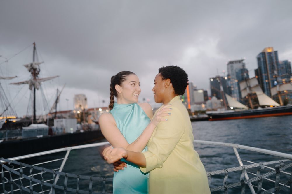 Couple sharing romantic moment on boat deck with city skyline in background.