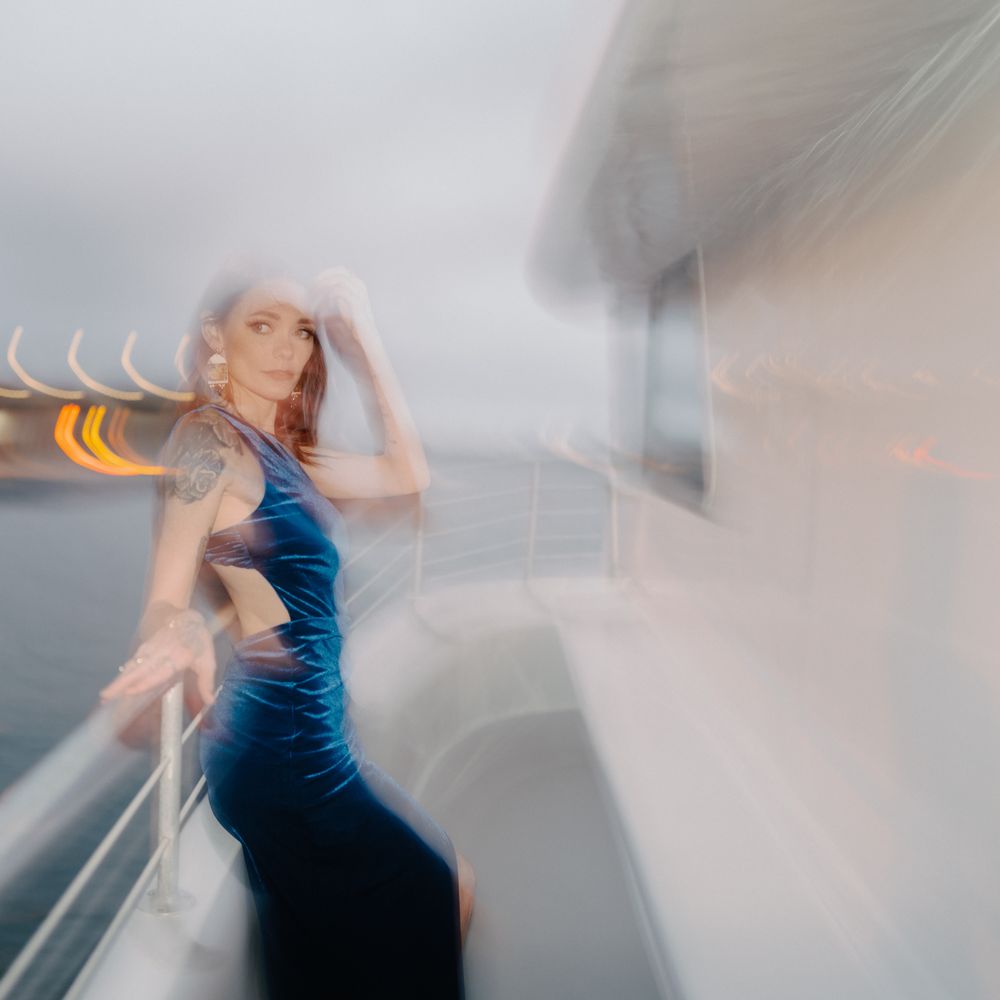 Artistic motion blur portrait of woman in blue dress on misty boat deck.