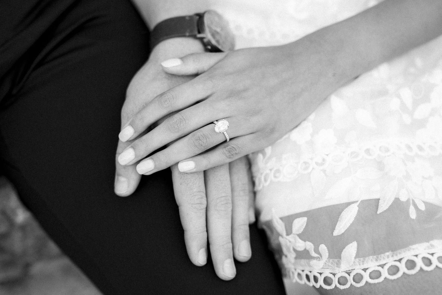 Black and white close-up of hands with wedding rings against white lace fabric.