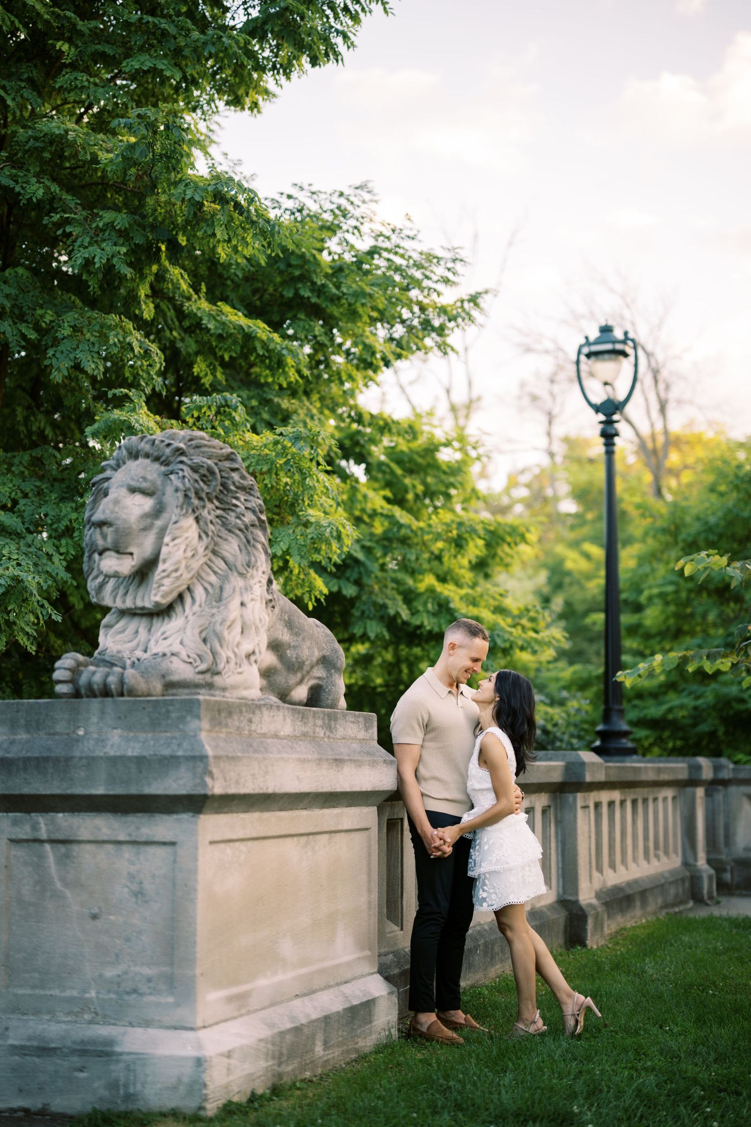 A romantic moment by a stone lion statue and lamp post in a lush green garden setting.