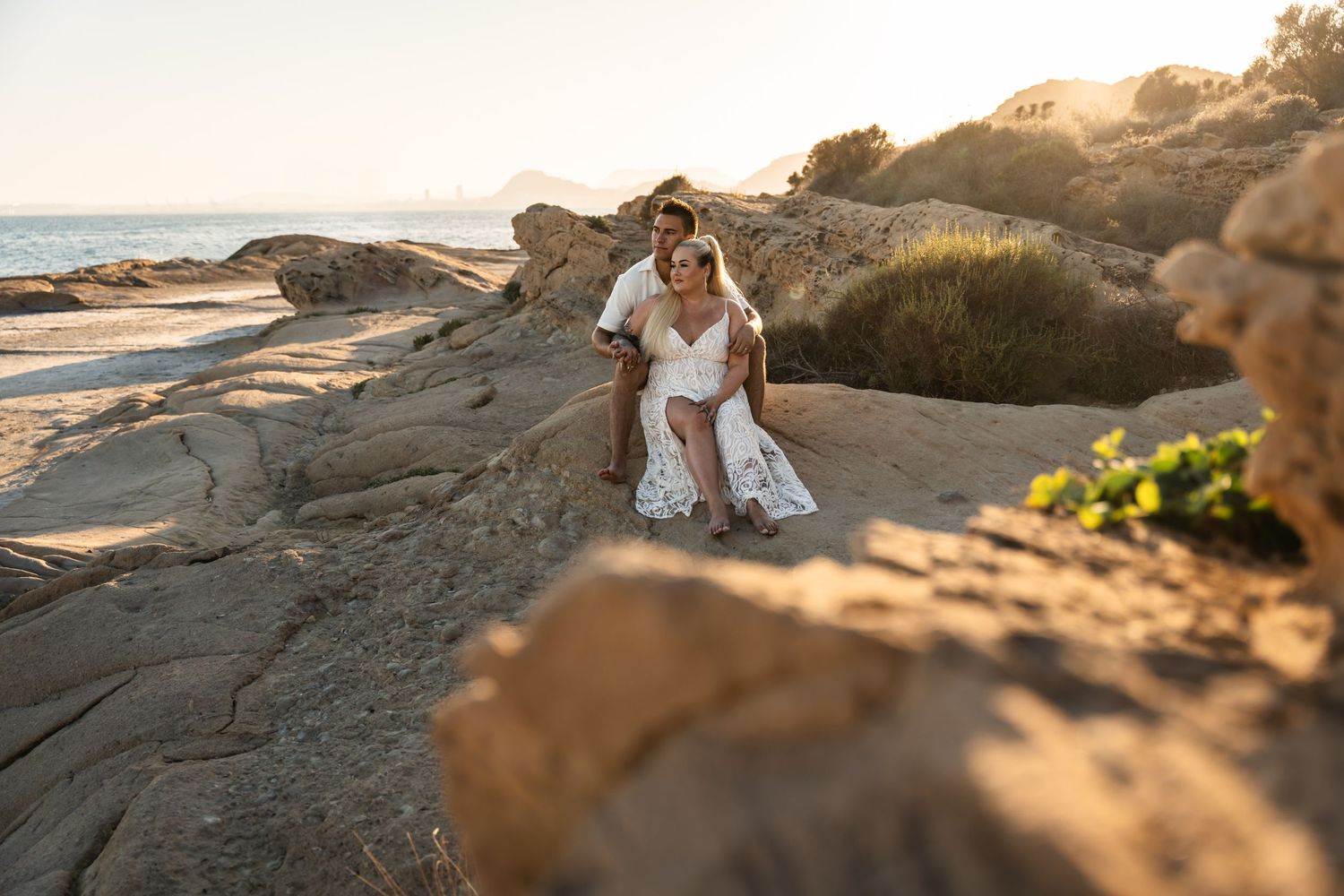 Couple sitting together in golden light on a rocky beach in Alicante Spain couples photo shoot