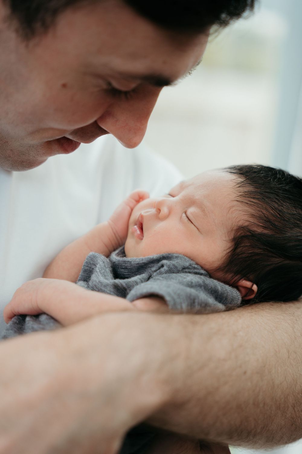 Parent gazing lovingly at sleeping newborn baby in grey clothing.