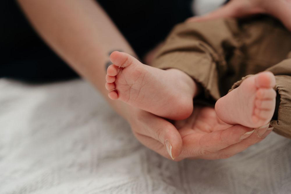 Tiny baby feet rest gently in adult hands on white bedding.