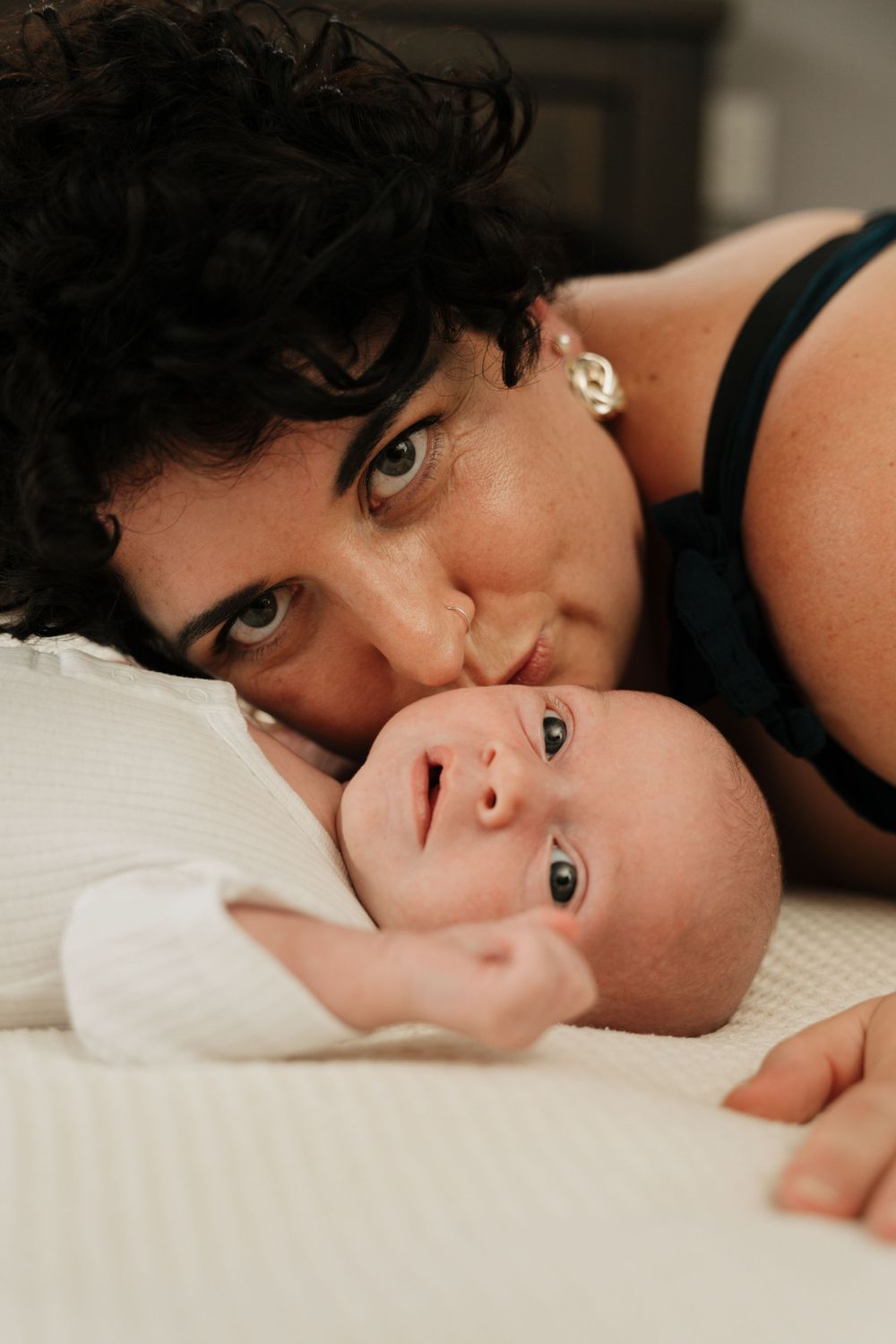 An intimate portrait of parent and baby laying together on white bedding.