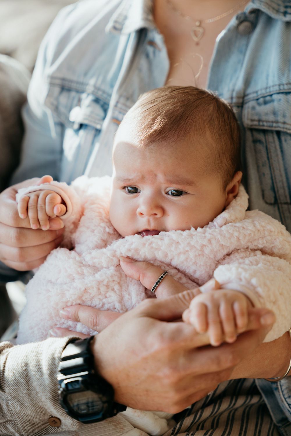 Baby in cozy white sweater being held securely while looking at camera.
