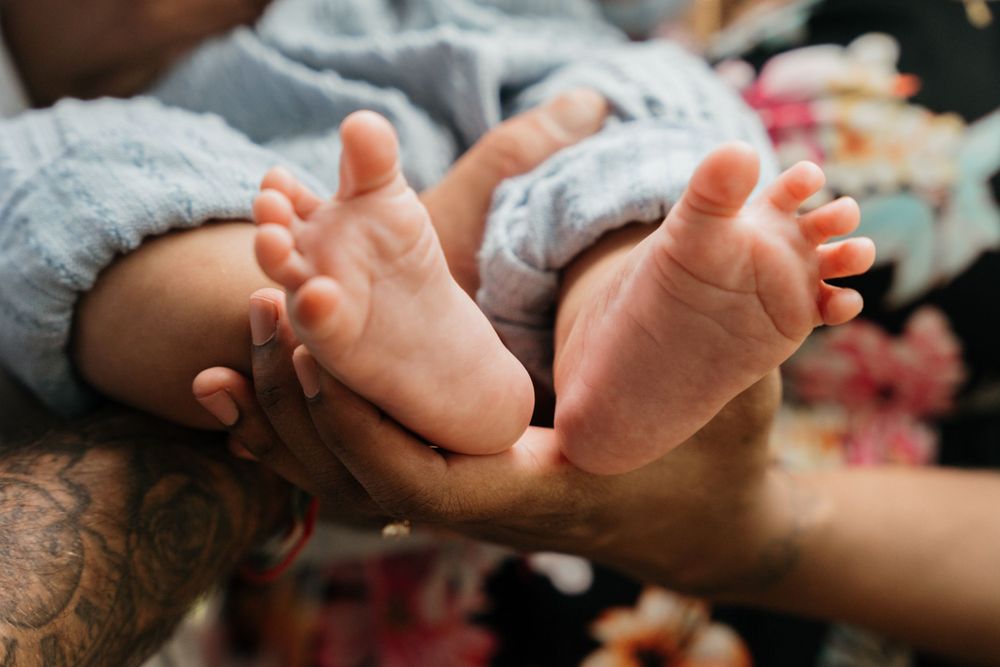 Close up of tiny newborn feet being gently held by tattooed hands.