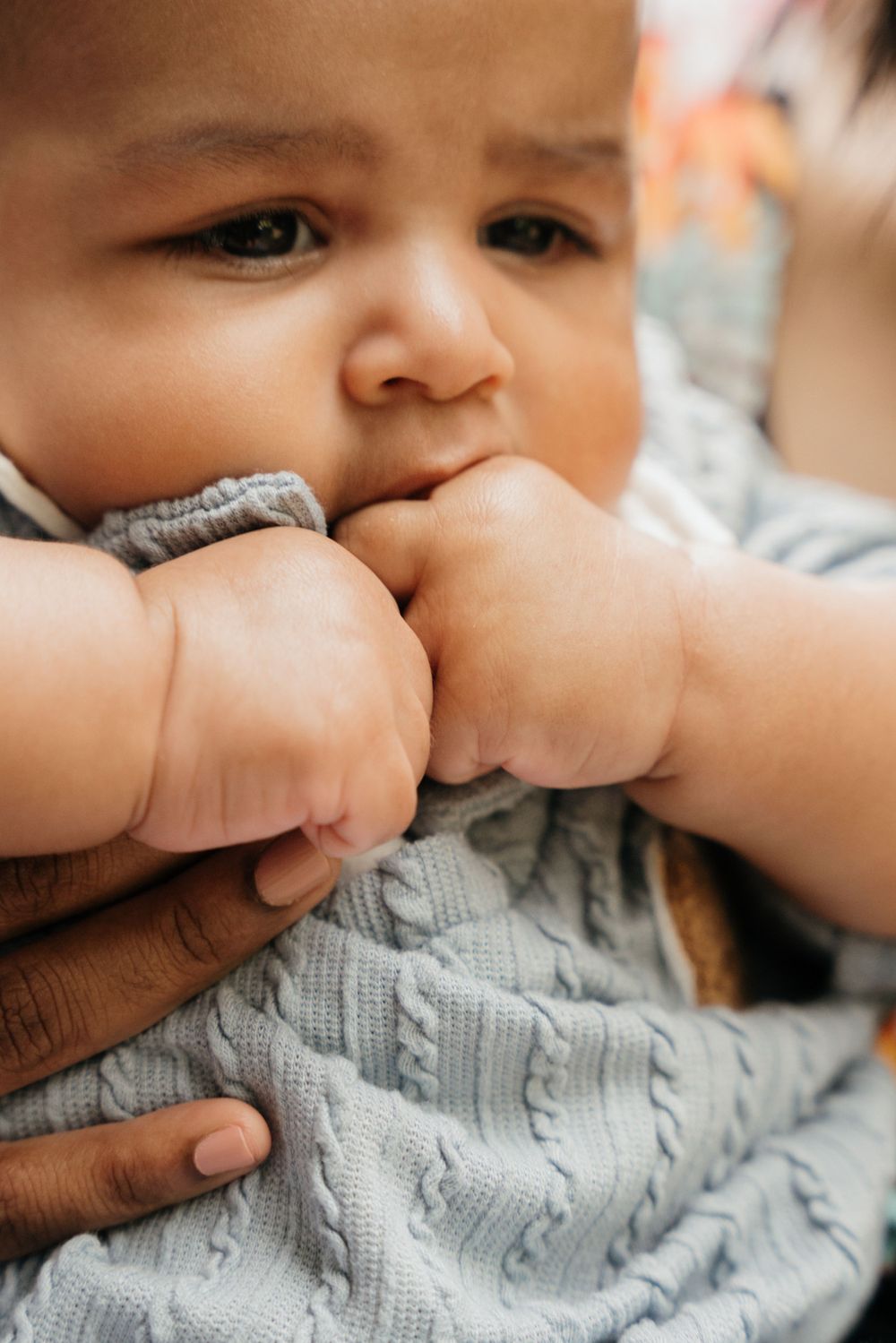 Close up of baby hands being held while wearing a grey knit sweater.