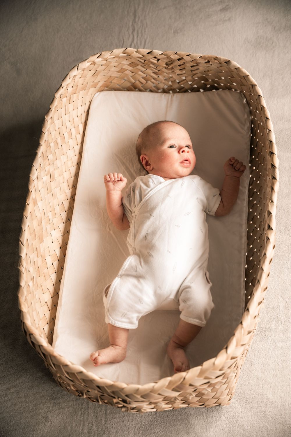 Newborn baby in white outfit lying peacefully in woven basket bassinet.