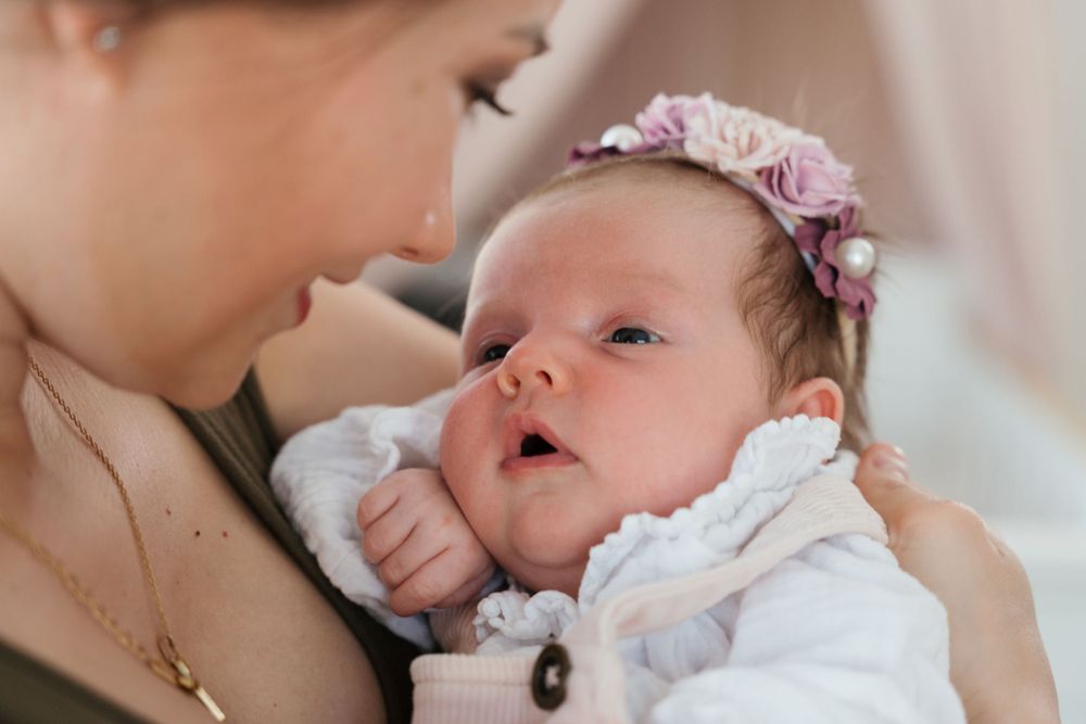 A baby wearing a floral headband rests peacefully in caring arms.