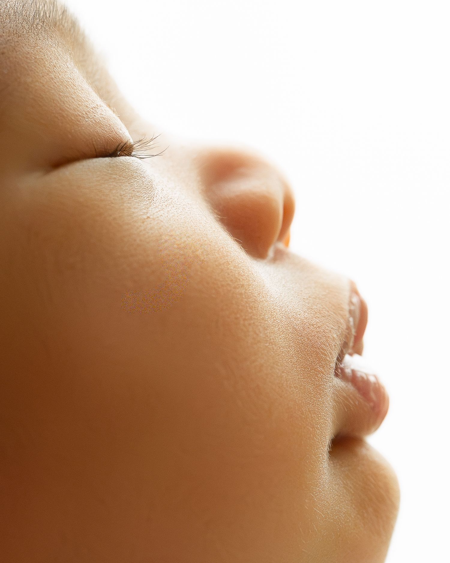 In a serene portrait against white backdrop, a woman in beige sweater gently cradles a sleeping newborn swaddled in cream.
