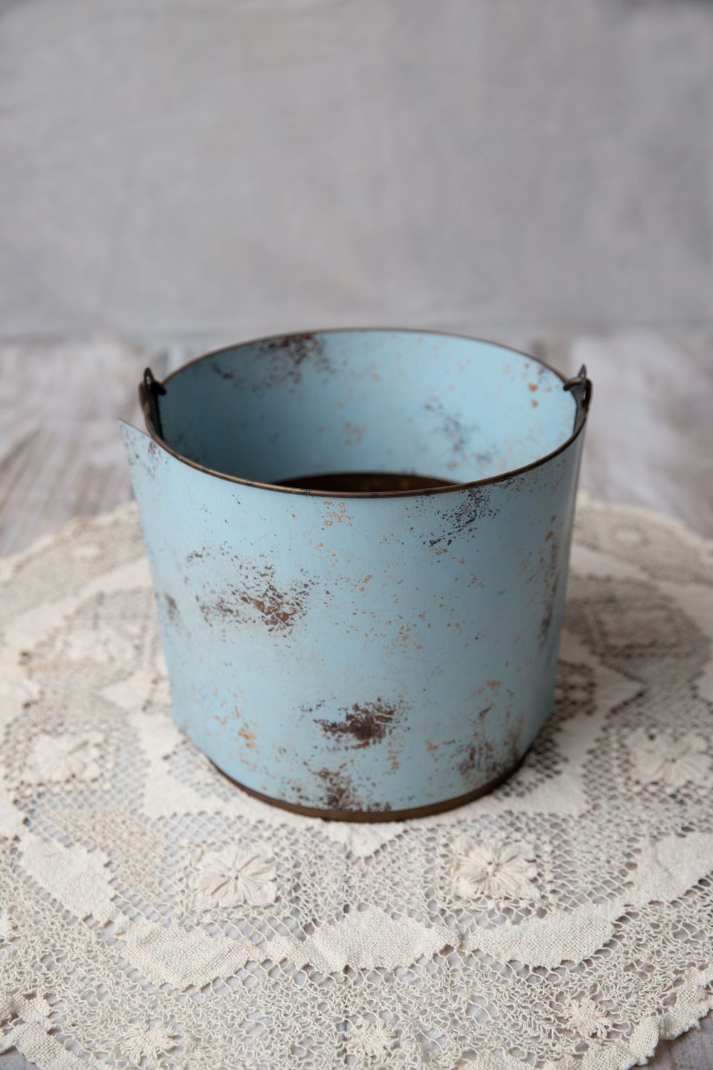 Distressed light blue metal bucket with rustic patina finish on a white lace doily.