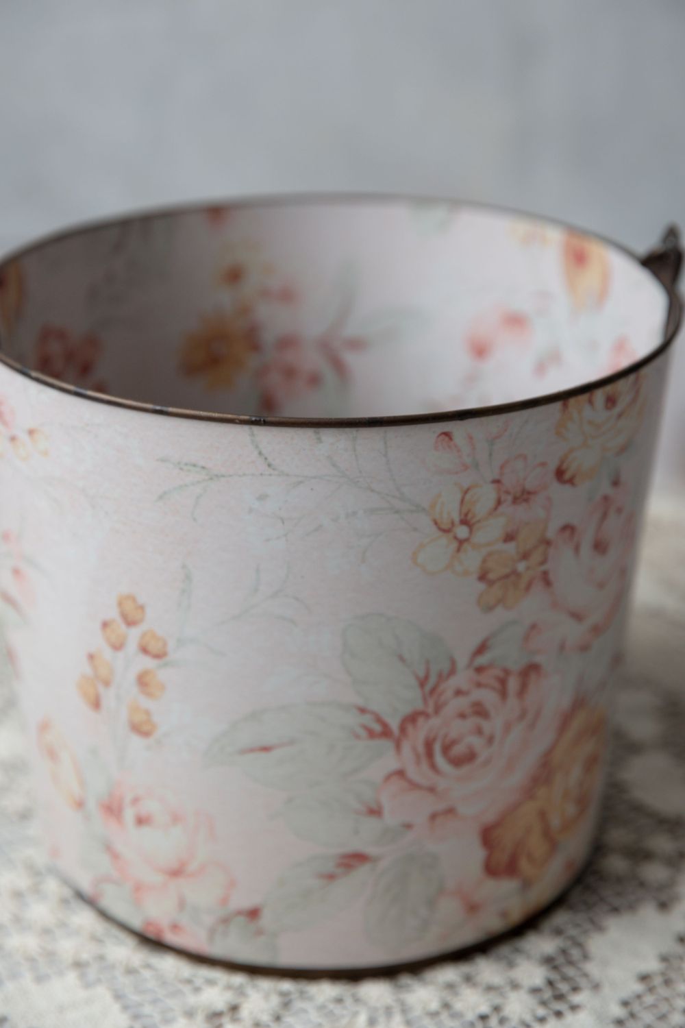 Vintage floral enamel cup with pink roses and soft pastel blooms on white background, shabby chic style.