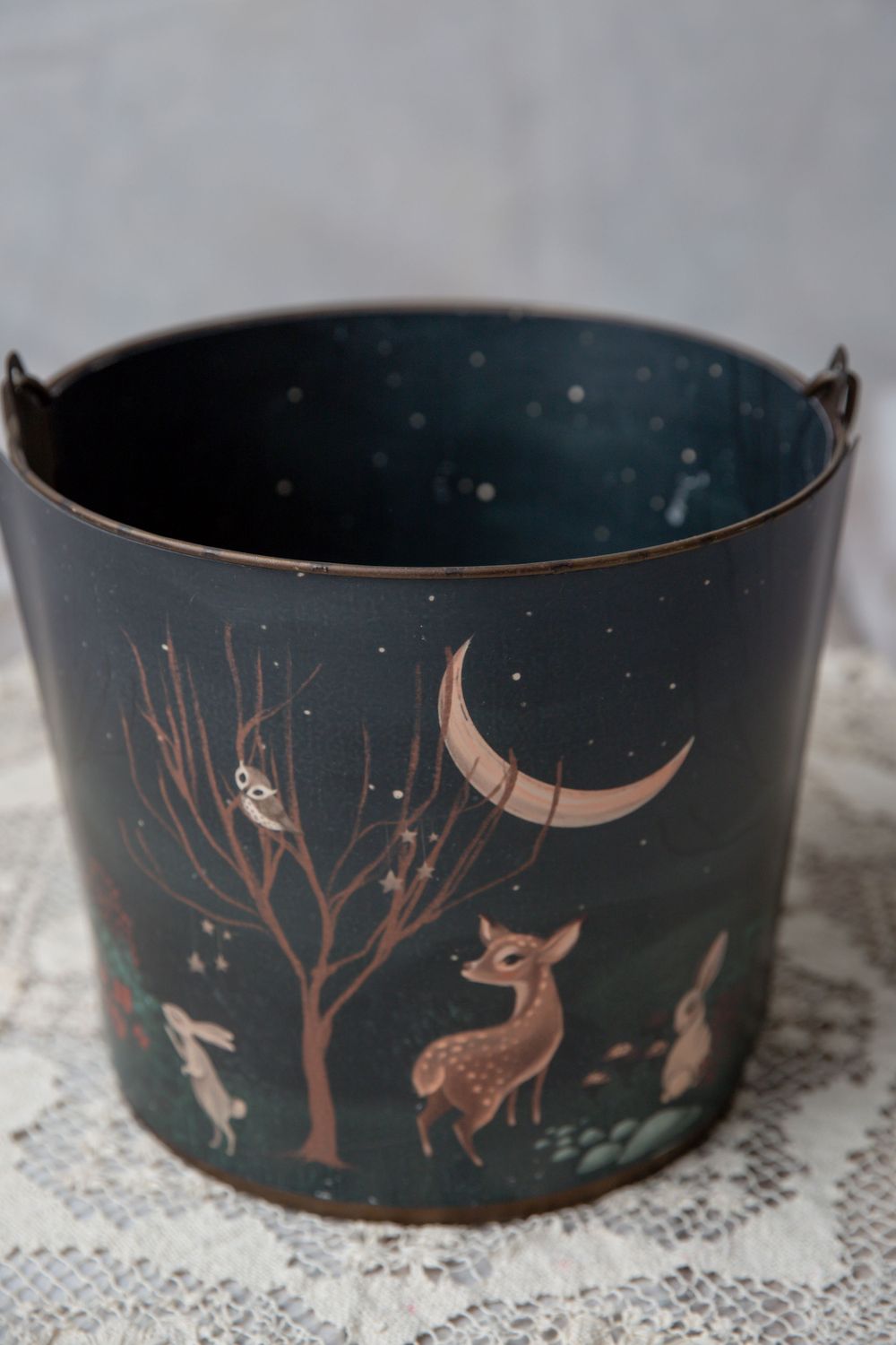 Dark teal metal bucket with enchanting forest scene featuring deer, rabbits, owl, crescent moon, and stars painted on exterior.
