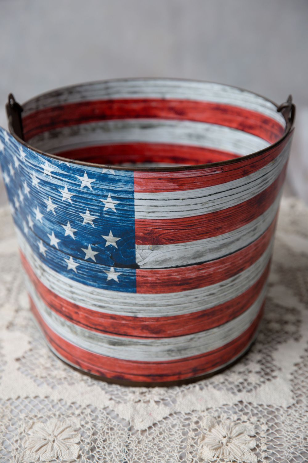 Rustic metal bucket with distressed American flag design featuring red, white, and blue stripes and stars.