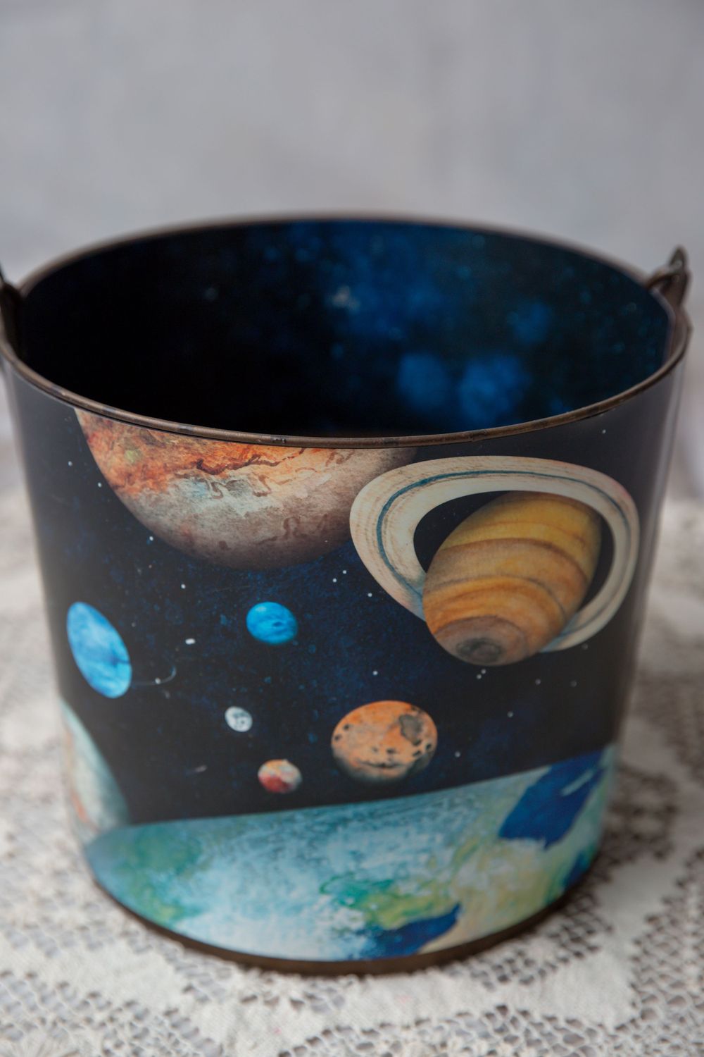 Dark metal bucket decorated with a vibrant solar system design featuring planets including Saturn and Earth.