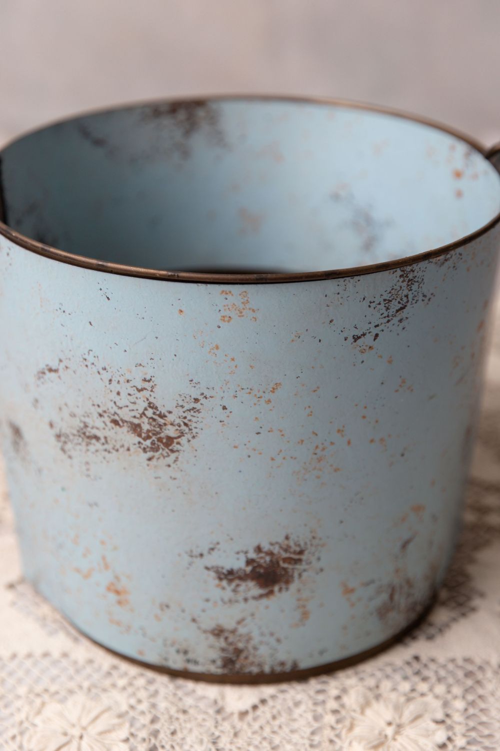 Vintage light blue distressed metal bucket with rustic worn patina on a lace doily.