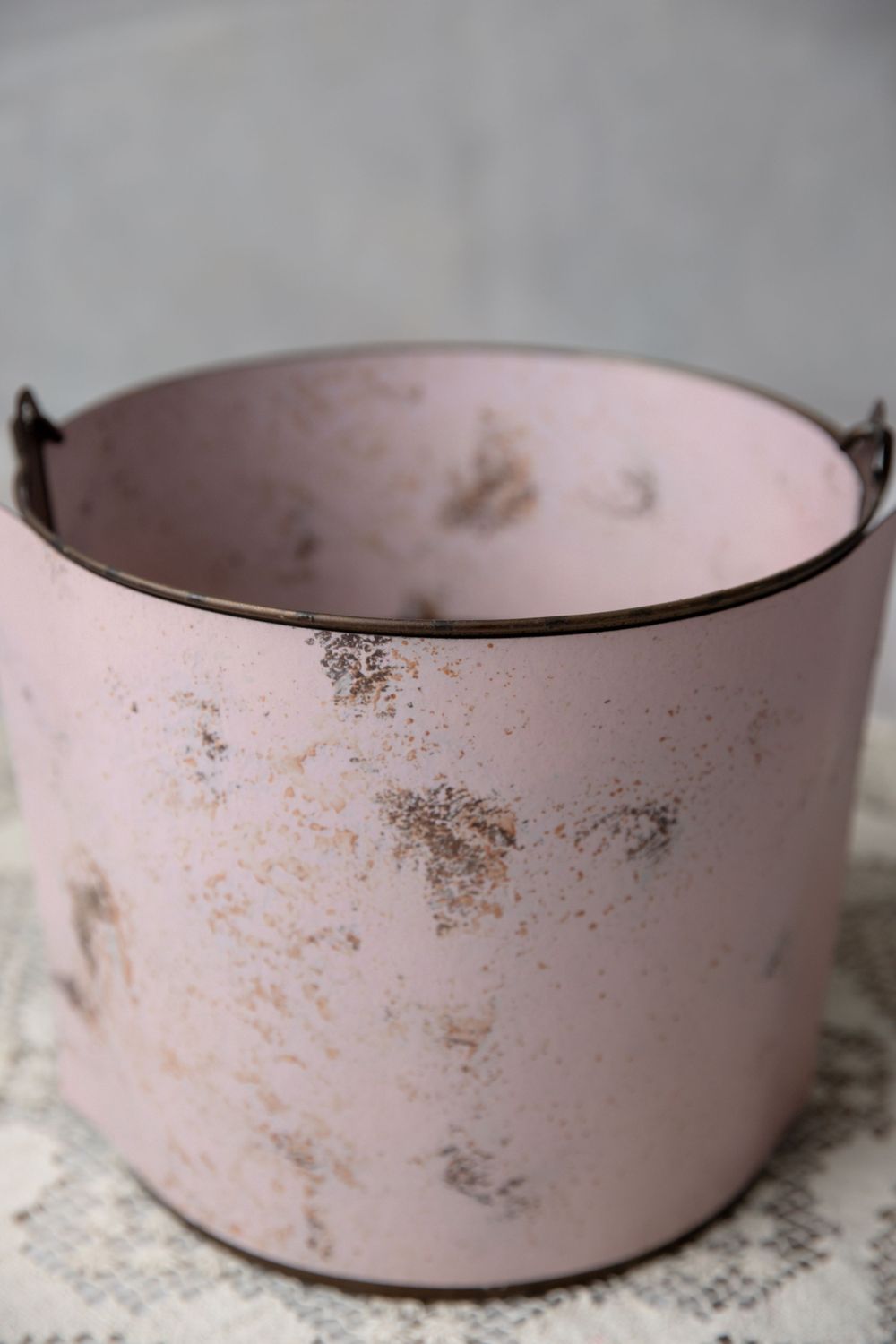 Vintage distressed pink metal bucket planter with rustic patina and small handles on gray background.