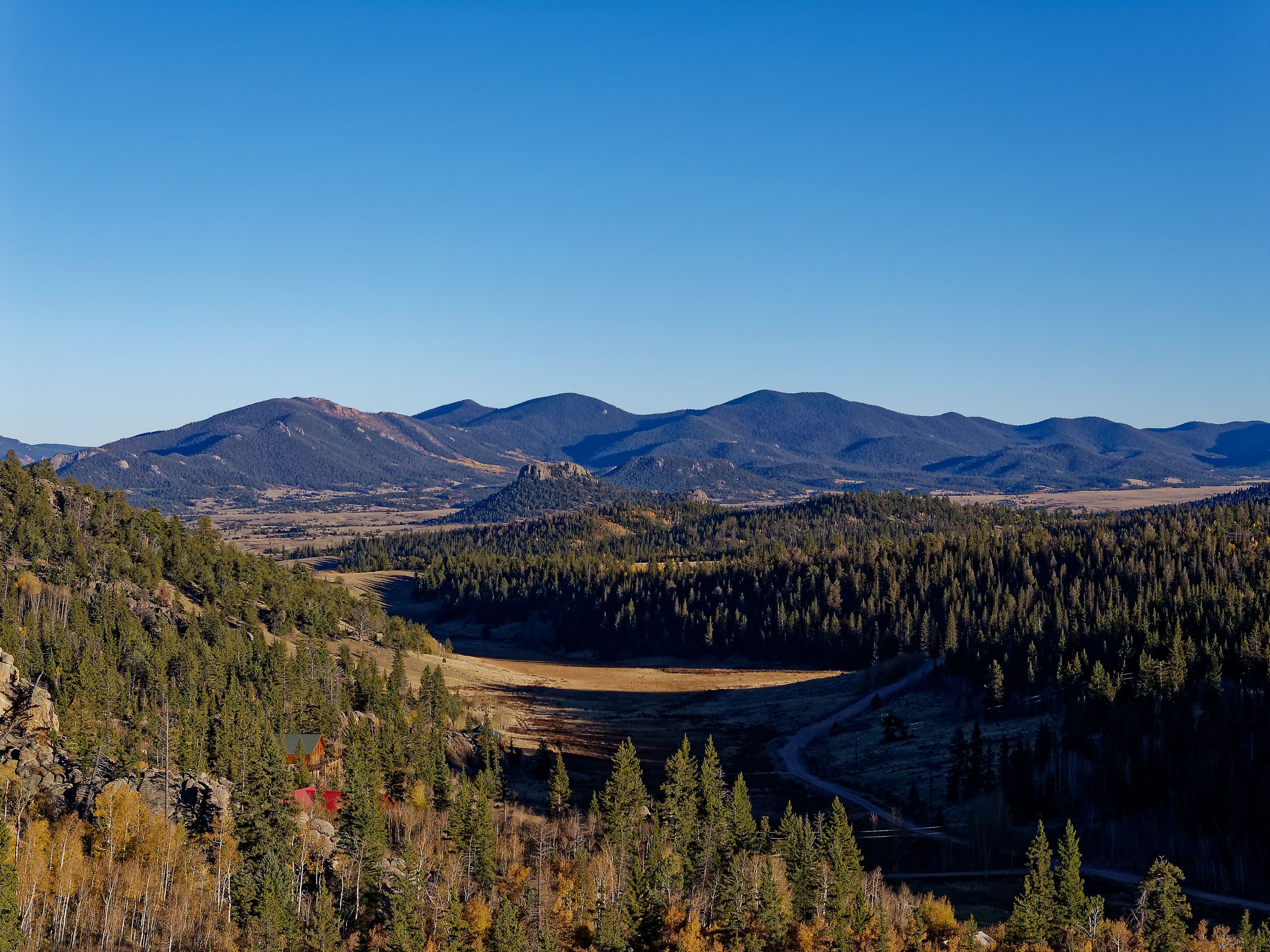 Scenic mountain vista overlooking a valley with dense pine forest and autumn colors.