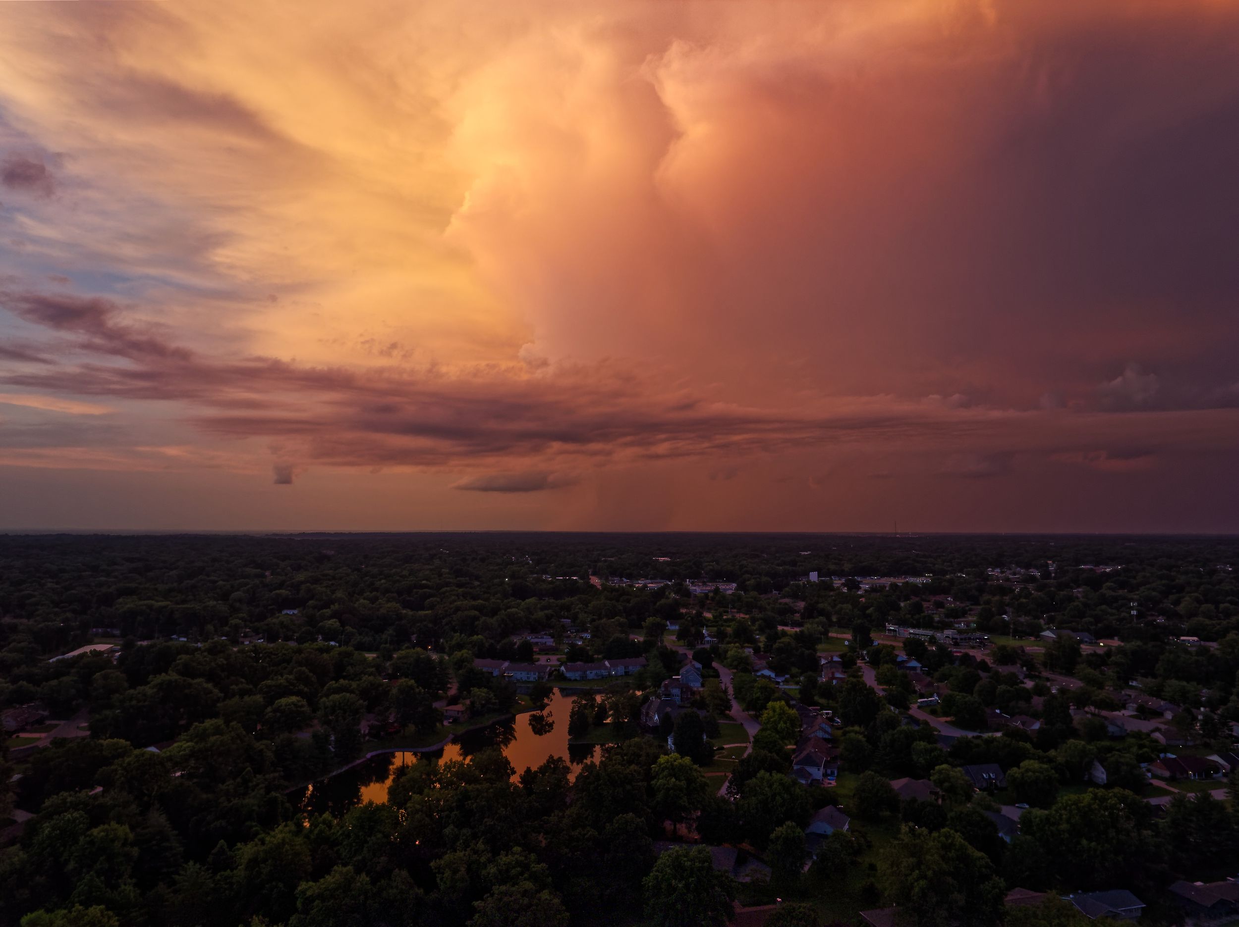 Aerial drone view of a suburban neighborhood under a dramatic orange and pink storm cloud sunset sky.