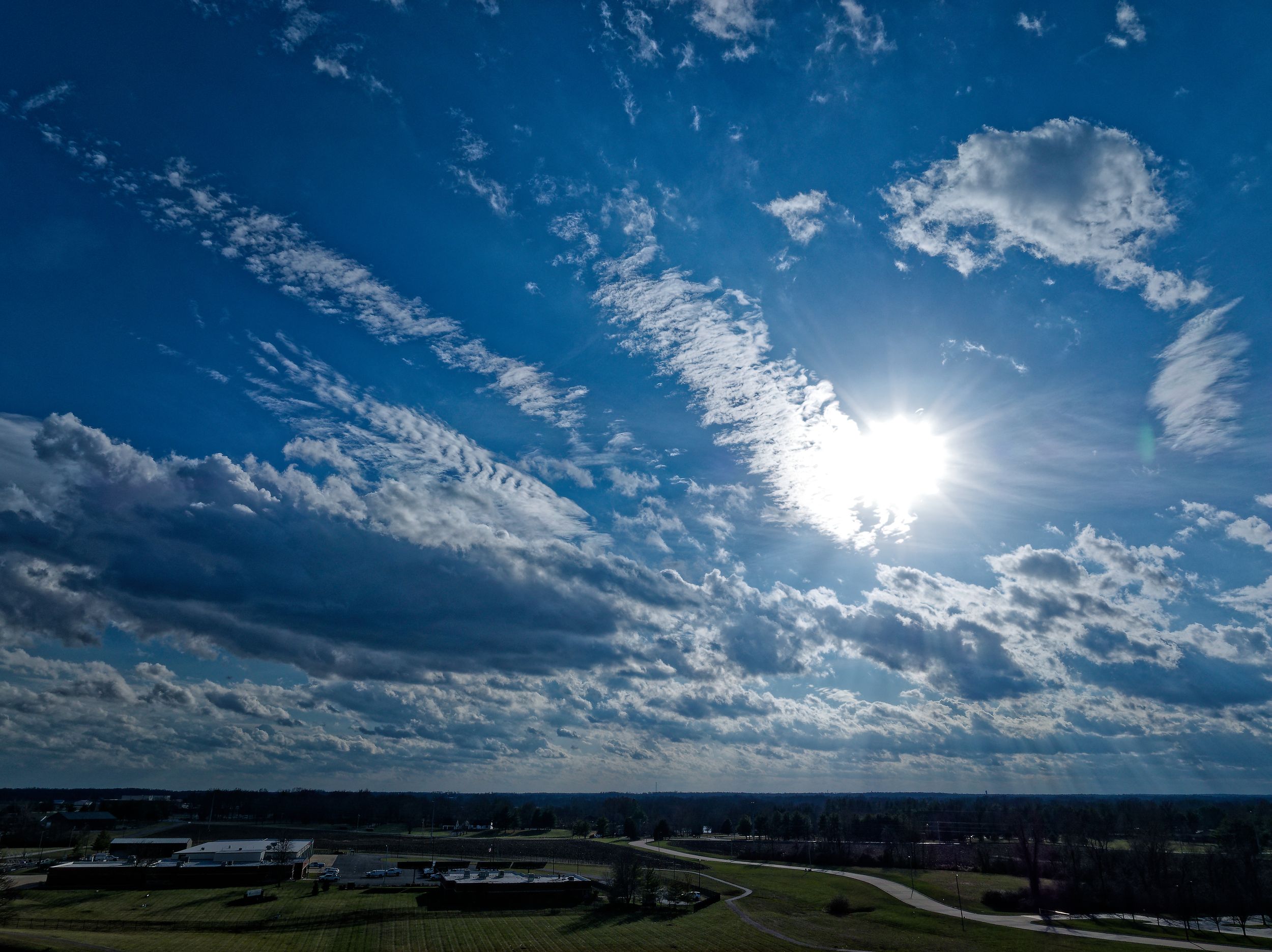 Dramatic blue sky with wispy clouds and bright sunlight over a rural landscape with winding roads.