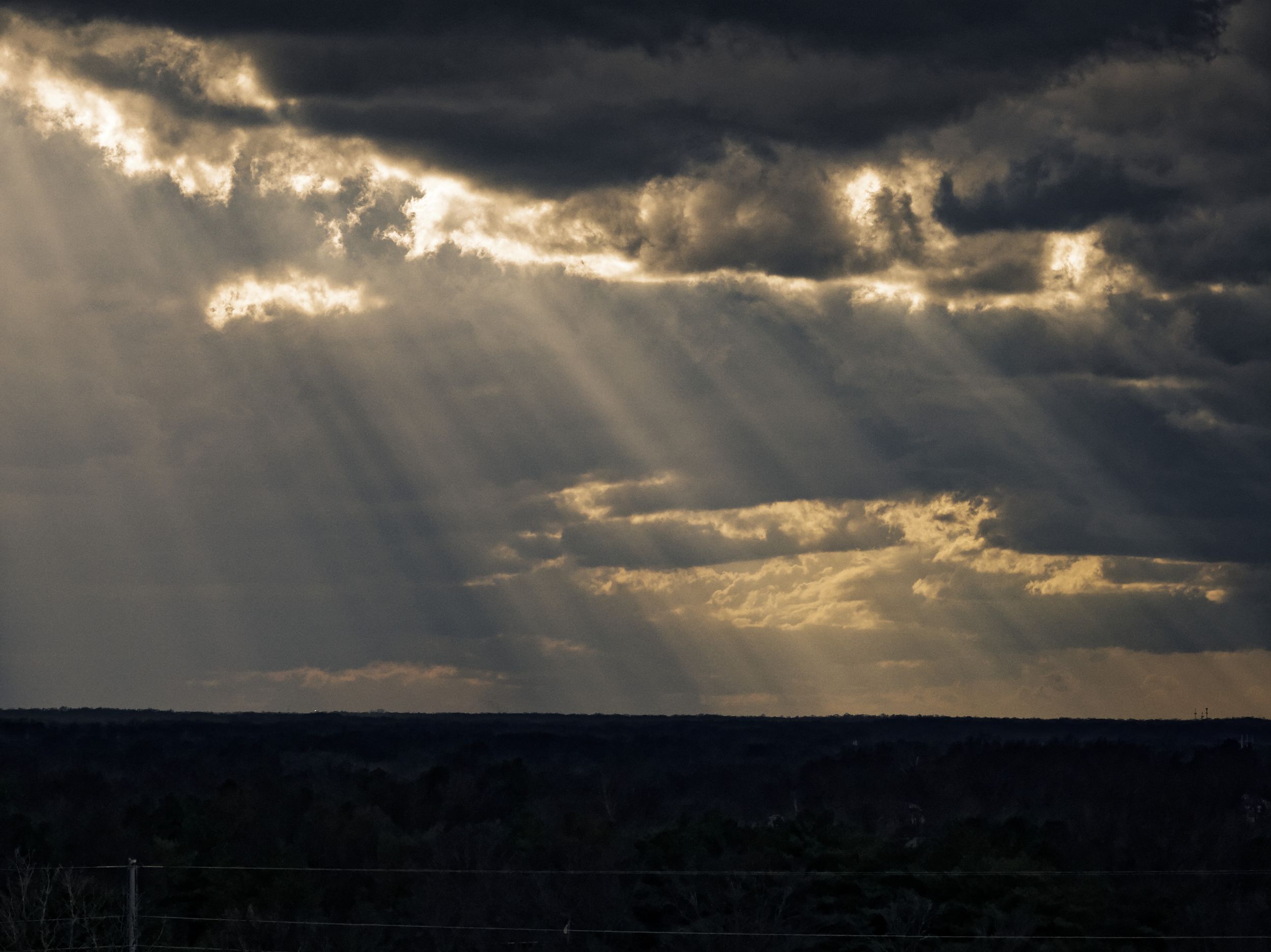 Sunbeams pierce through dark storm clouds creating dramatic crepuscular rays over a distant horizon.