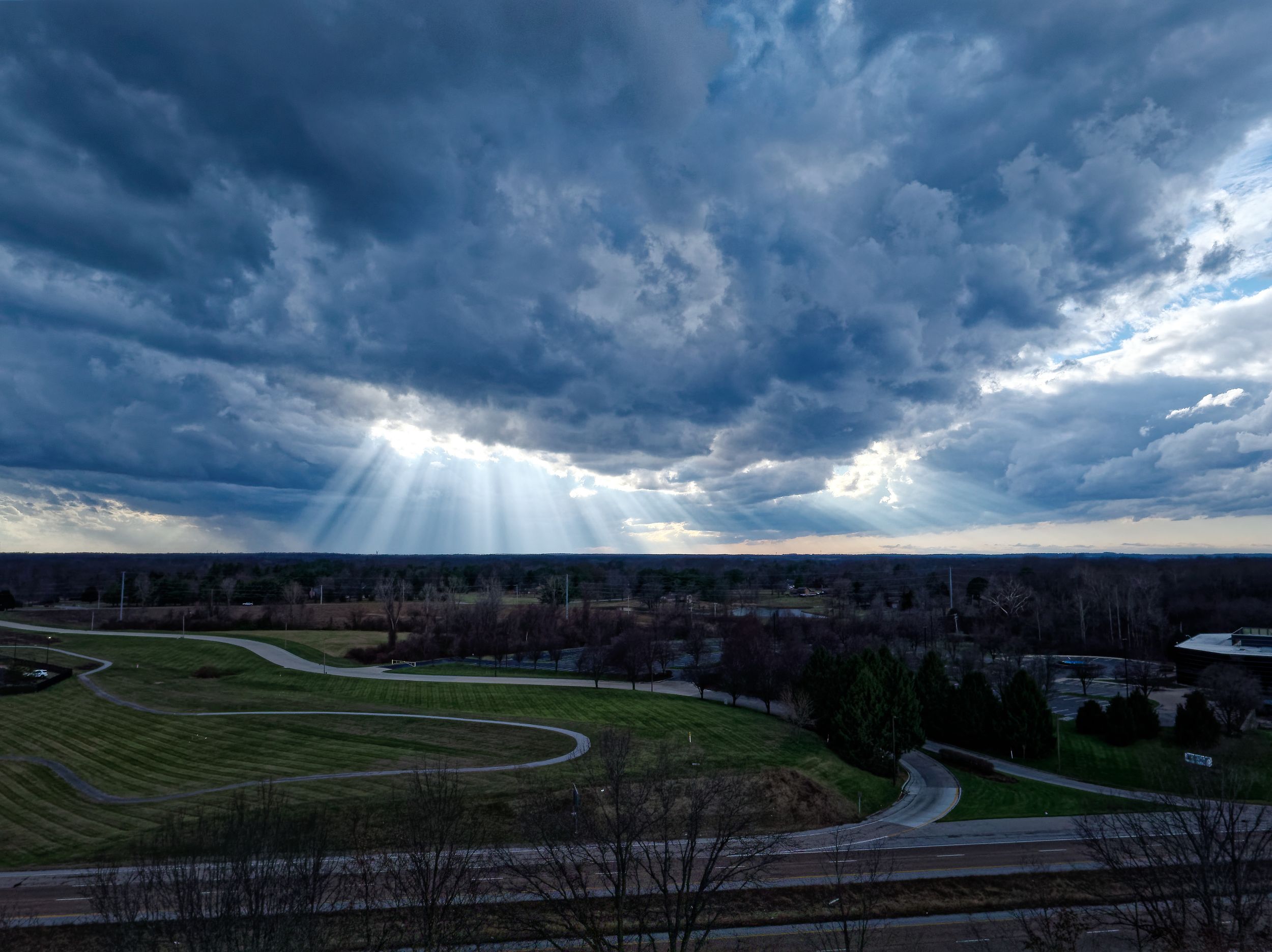 Sunrays break through stormy clouds illuminating a curved track and green landscape below.