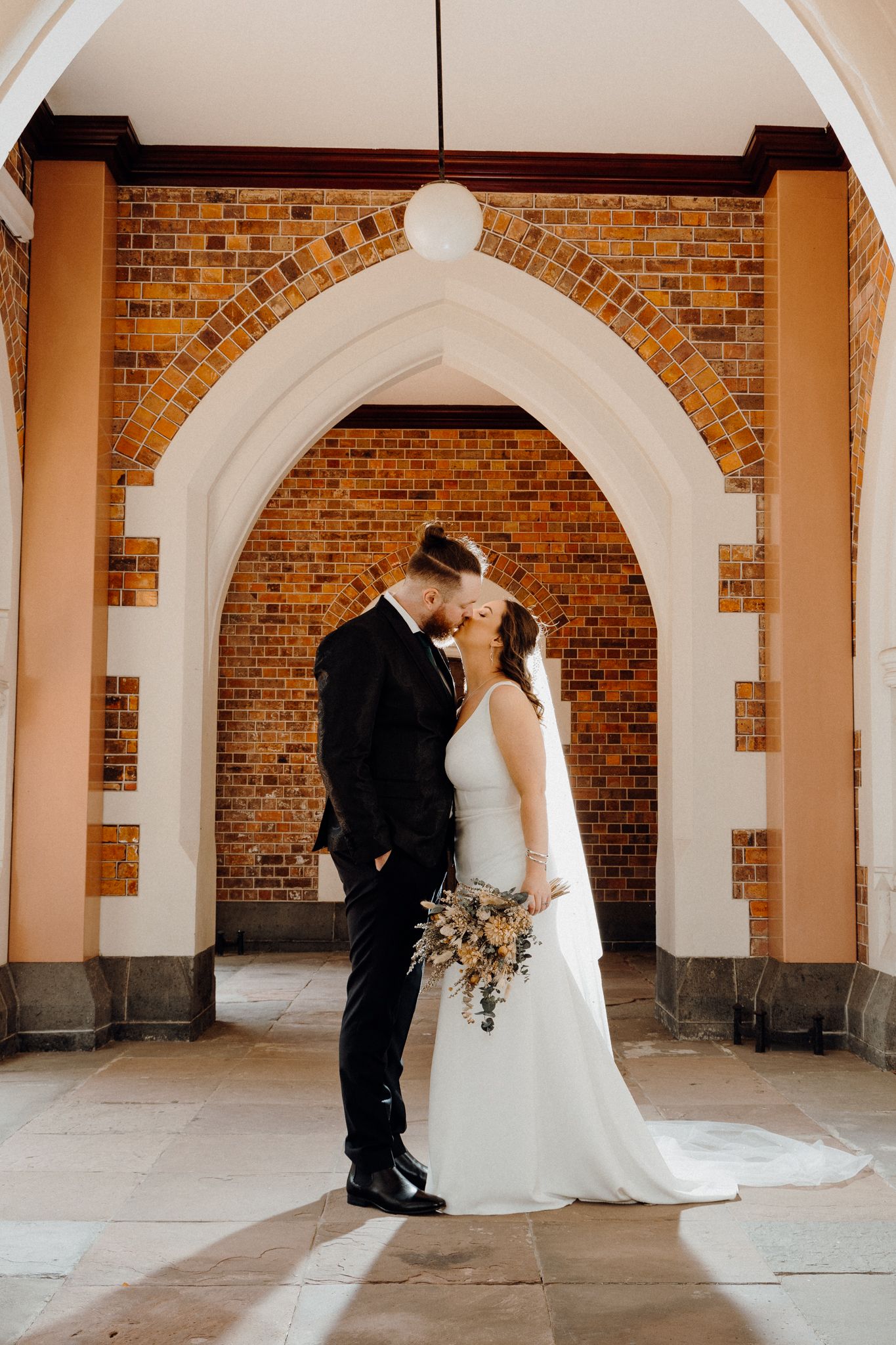 A romantic wedding couple kisses under a brick archway captured by Apertured Media Auckland Wedding Photographer.