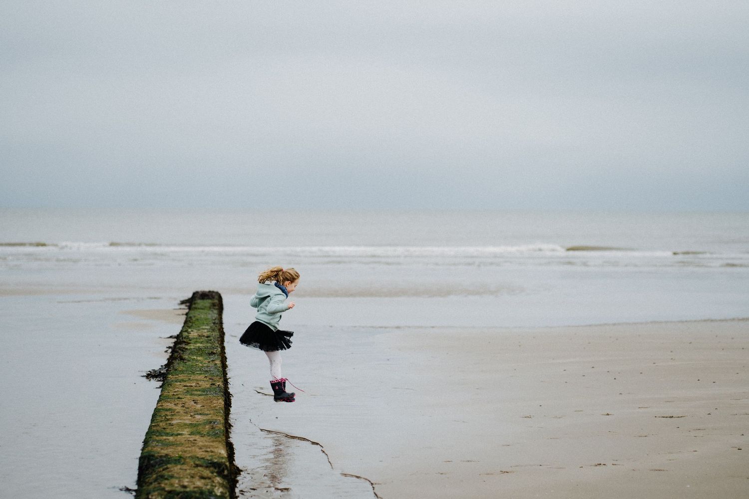A person stands by a wooden breakwater on a misty beach with rolling waves in the background.