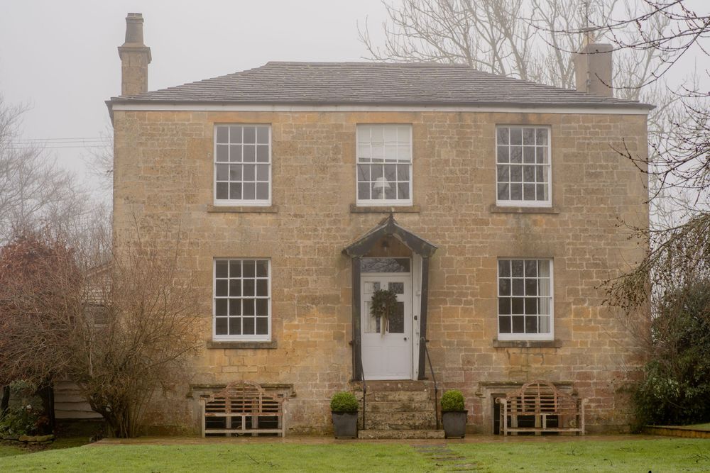 Symmetrical Georgian style stone house with white sash windows and central doorway flanked by wooden benches on the porch.