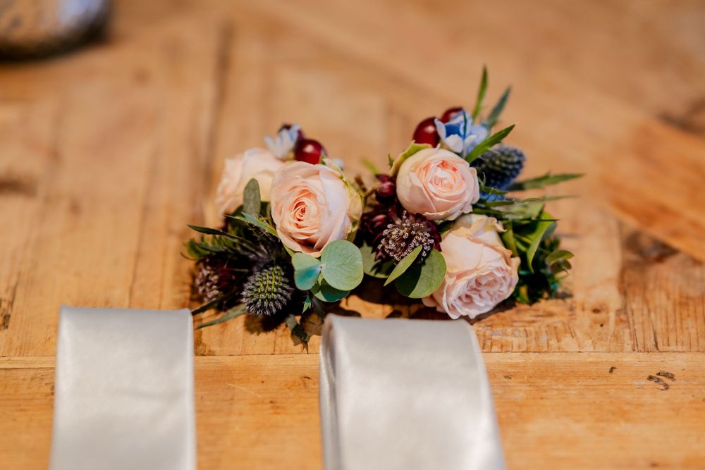 Delicate pink roses and greenery arranged in a rustic wedding bouquet on a wooden surface with white ribbon.