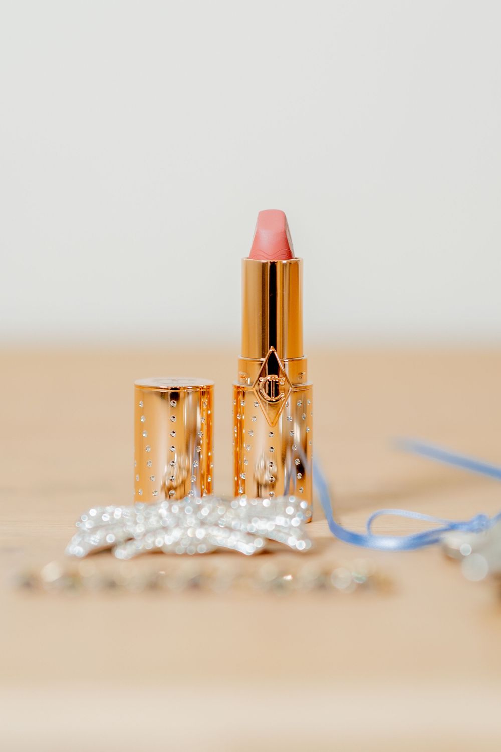 Elegant gold lipstick tube displayed with pearl accessories on a neutral background.