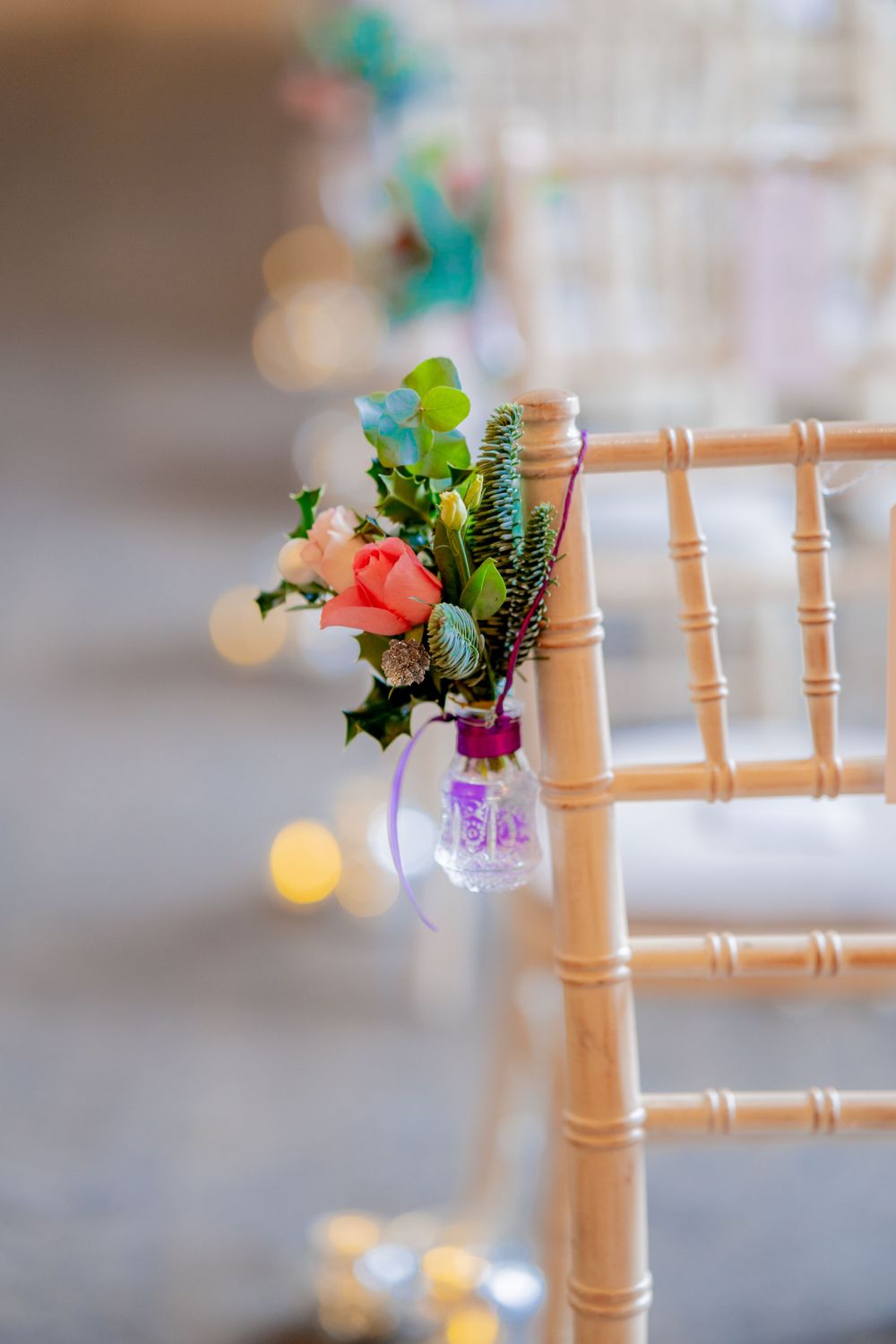 Small floral arrangement in a glass vase hangs decoratively from a wooden chiavari chair at a wedding reception.