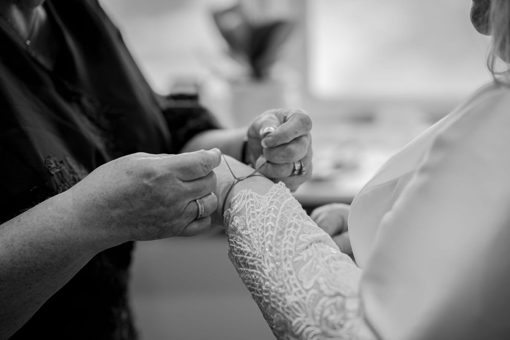 A close-up black and white shot of hands adjusting an elegant lacey bridal sleeve detail during wedding preparations.