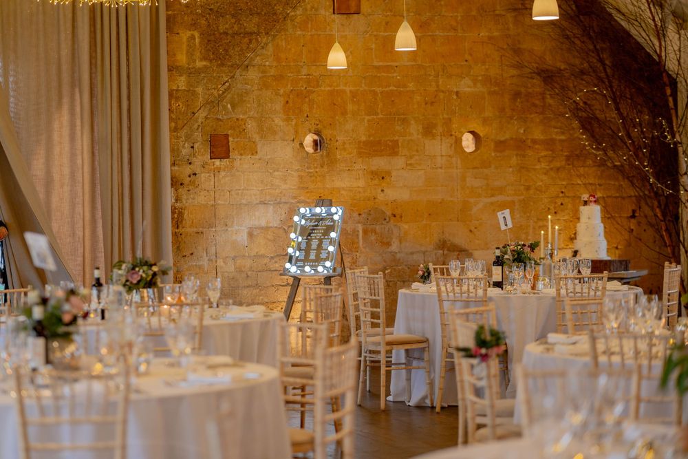 Elegant wedding reception venue with stone walls, hanging lights, and white-draped tables in rustic setting.