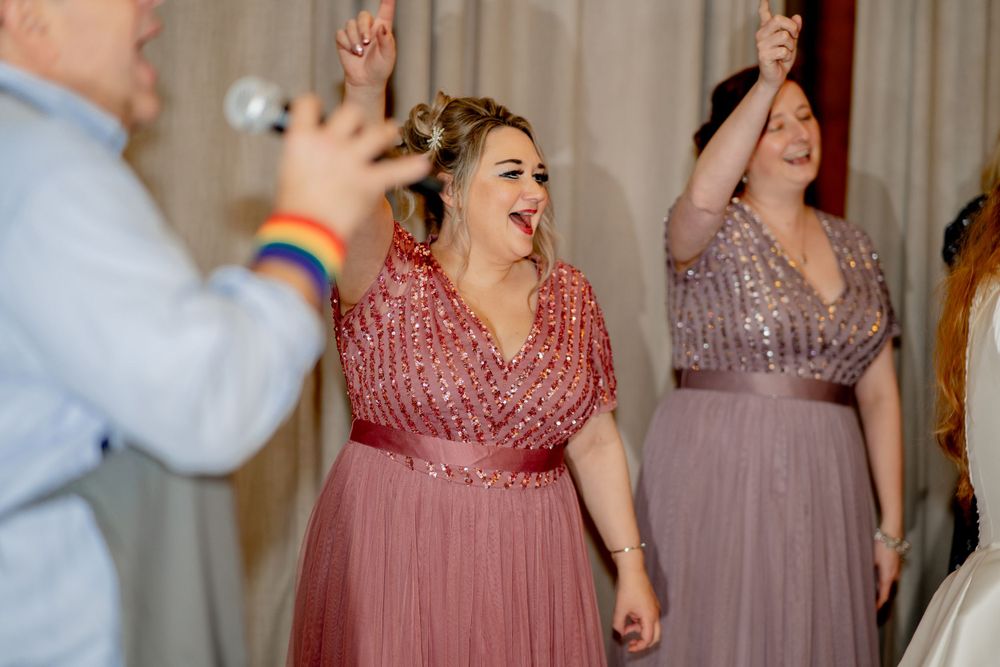 Wedding guests dancing and celebrating in pink formal attire at an indoor reception.