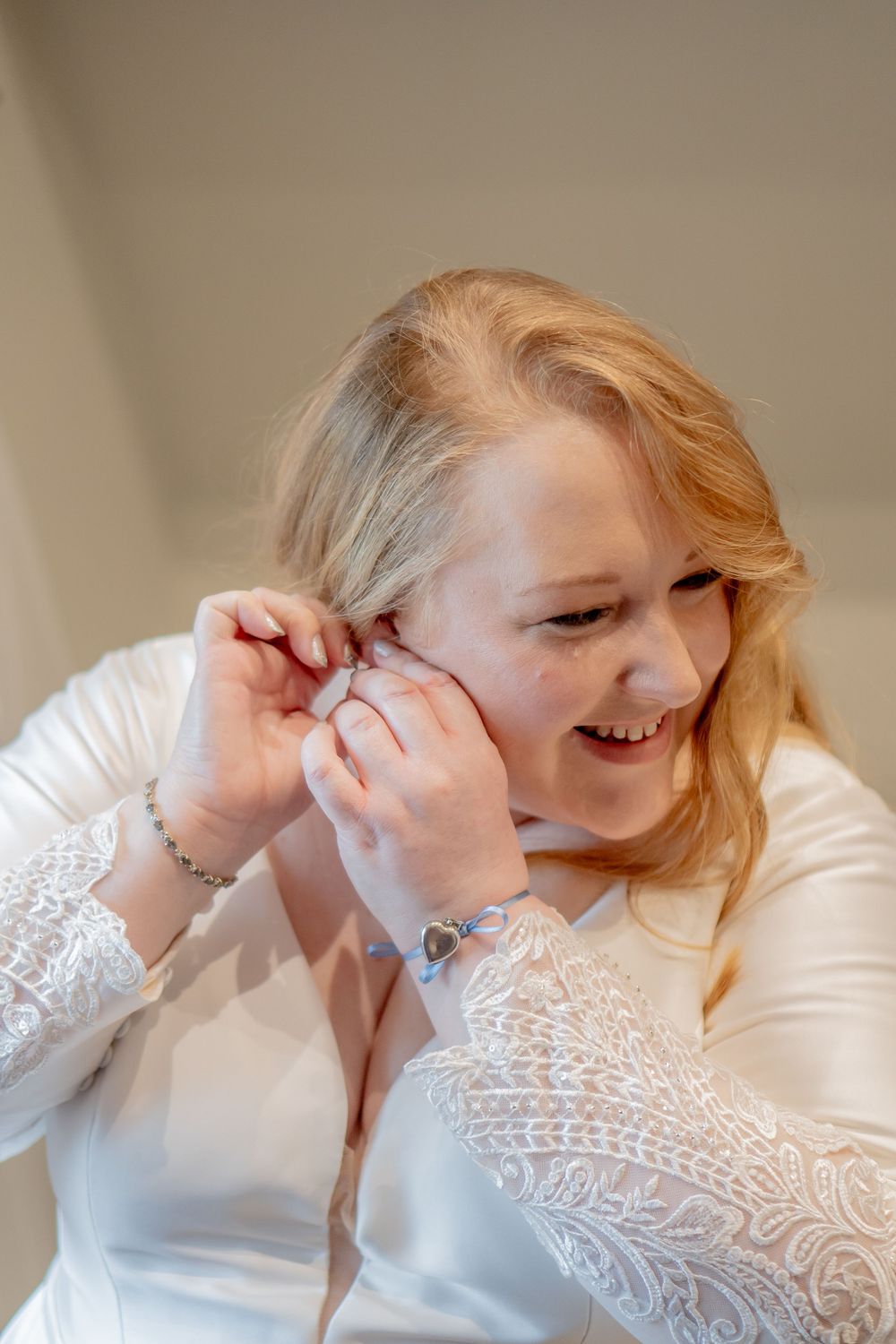 A person wearing a white lace dress smiles while adjusting something near their ear.