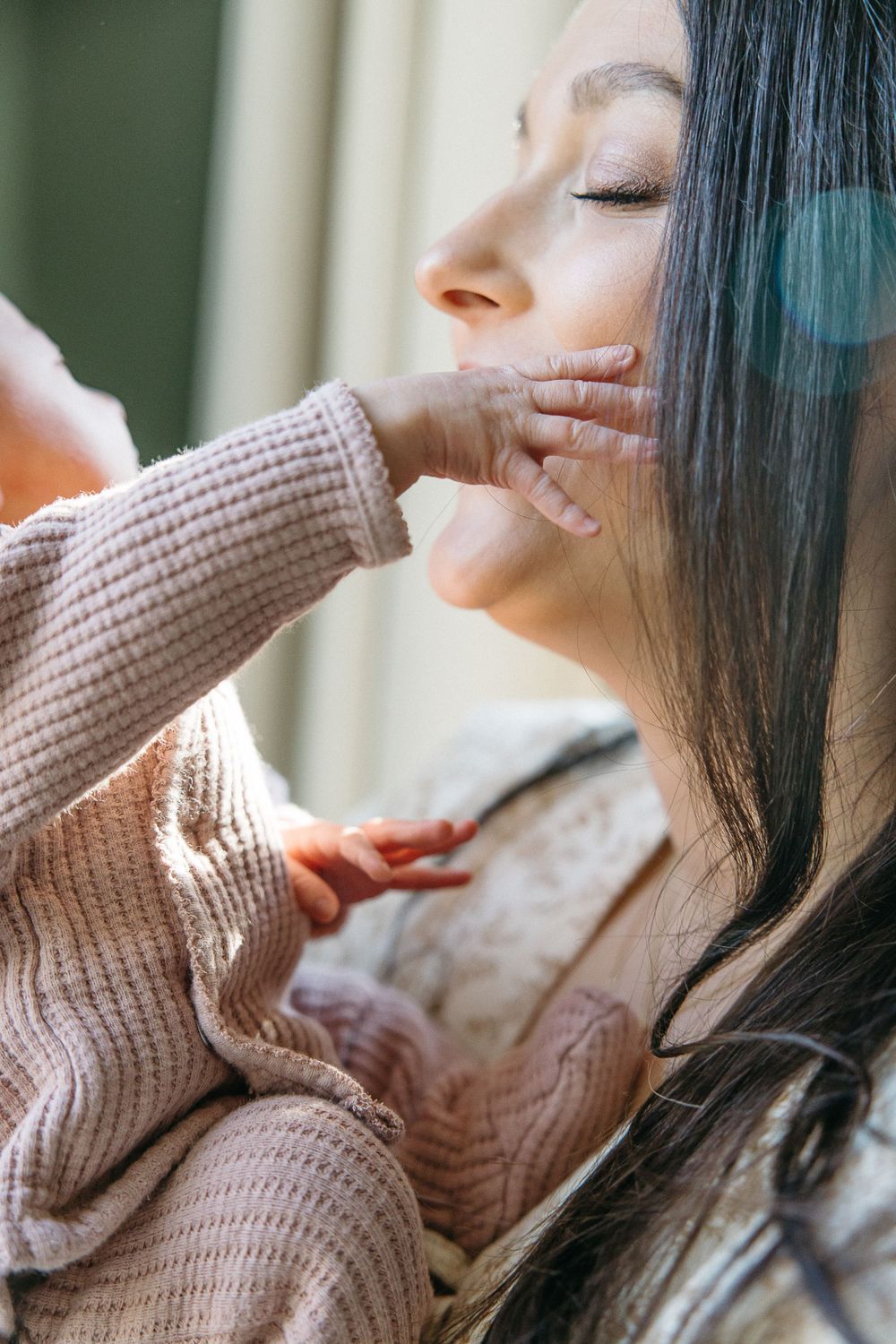 Woman in beige knit sweater relaxes with eyes closed while gently touching her chin in soft natural light.