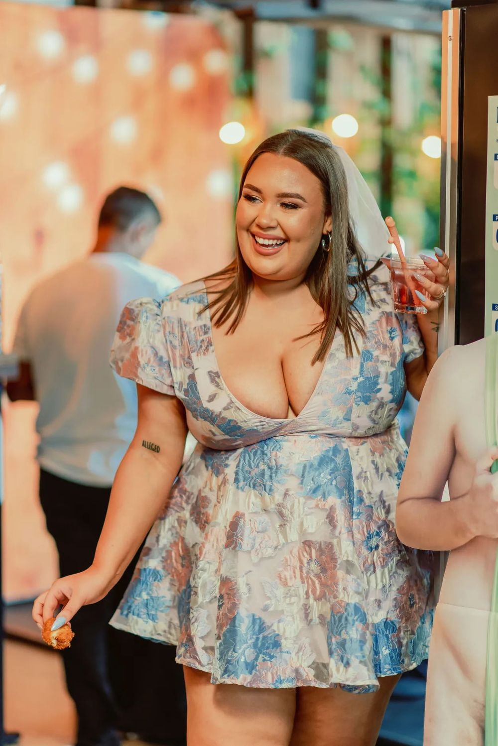 Woman in blue and white floral dress smiling and posing at indoor event.