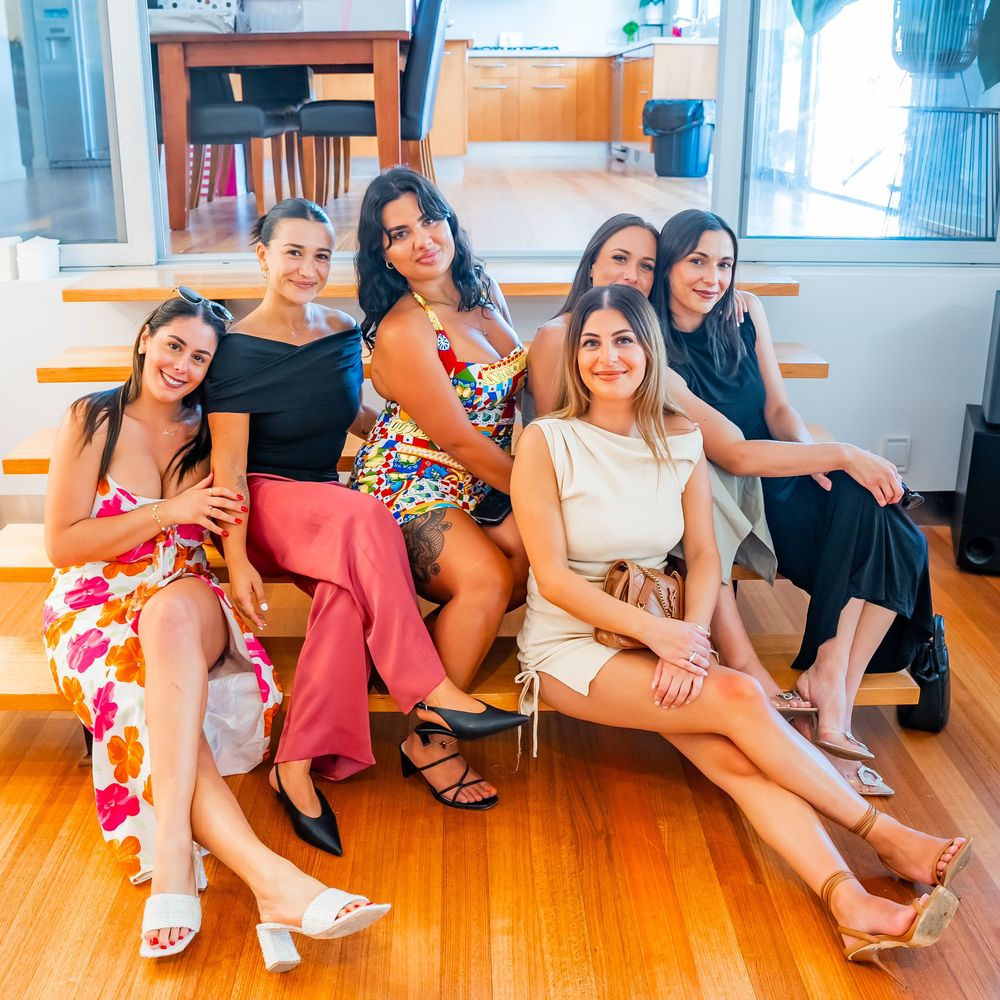 A panoramic photo of people sitting on a hardwood floor in a bright room with large windows.