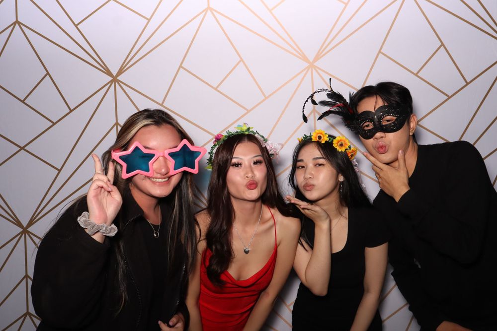 Friends posing with fun glasses and props against geometric pattern background.