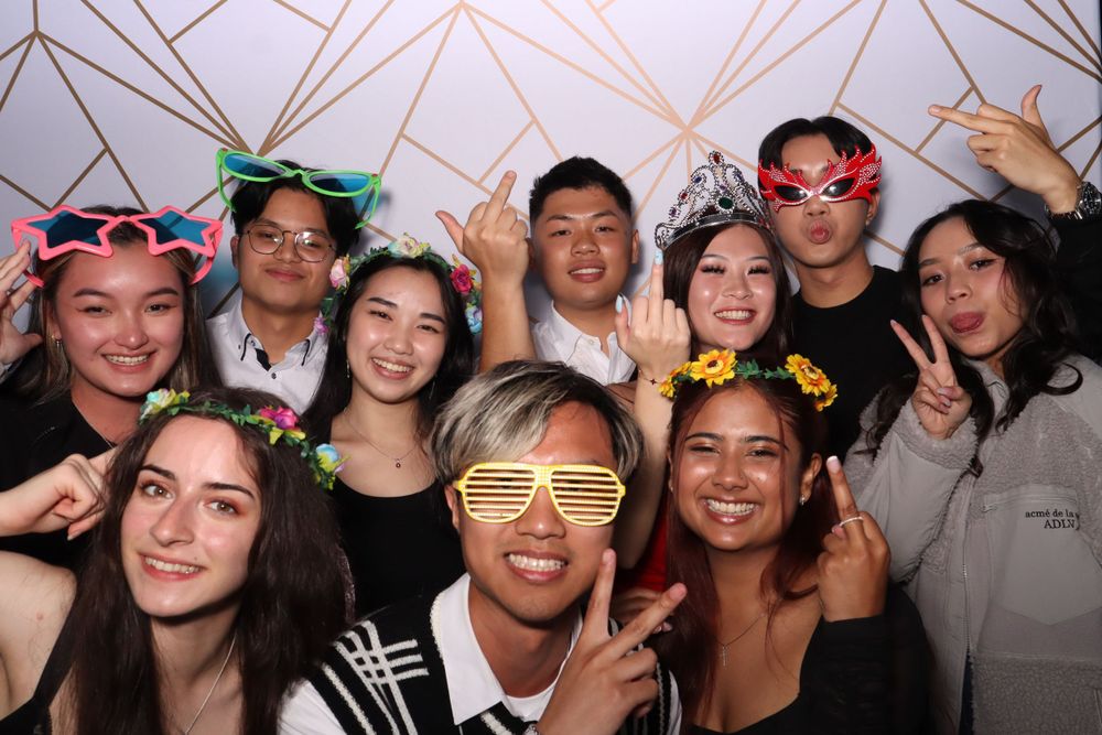Group of friends posing with fun party glasses and props against a geometric patterned backdrop.