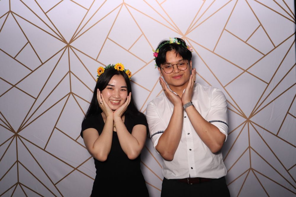 Two people pose with hands on cheeks against a geometric patterned wall.