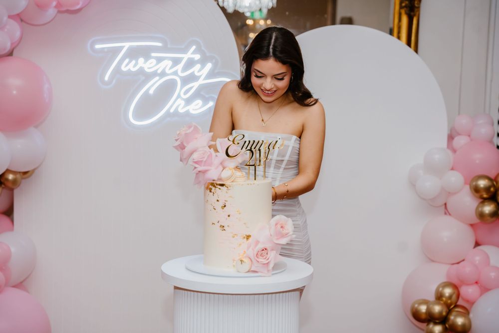 Woman in elegant dress admires decorated cake at 21st birthday celebration.