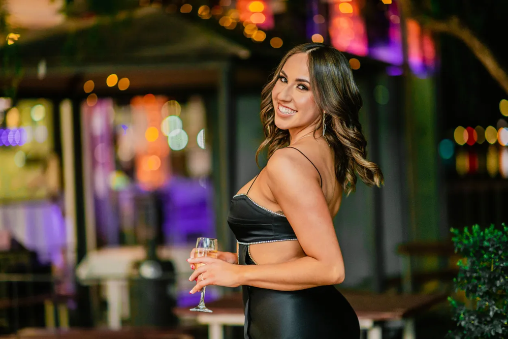 Woman in black dress smiles at nighttime event with colorful lighting.