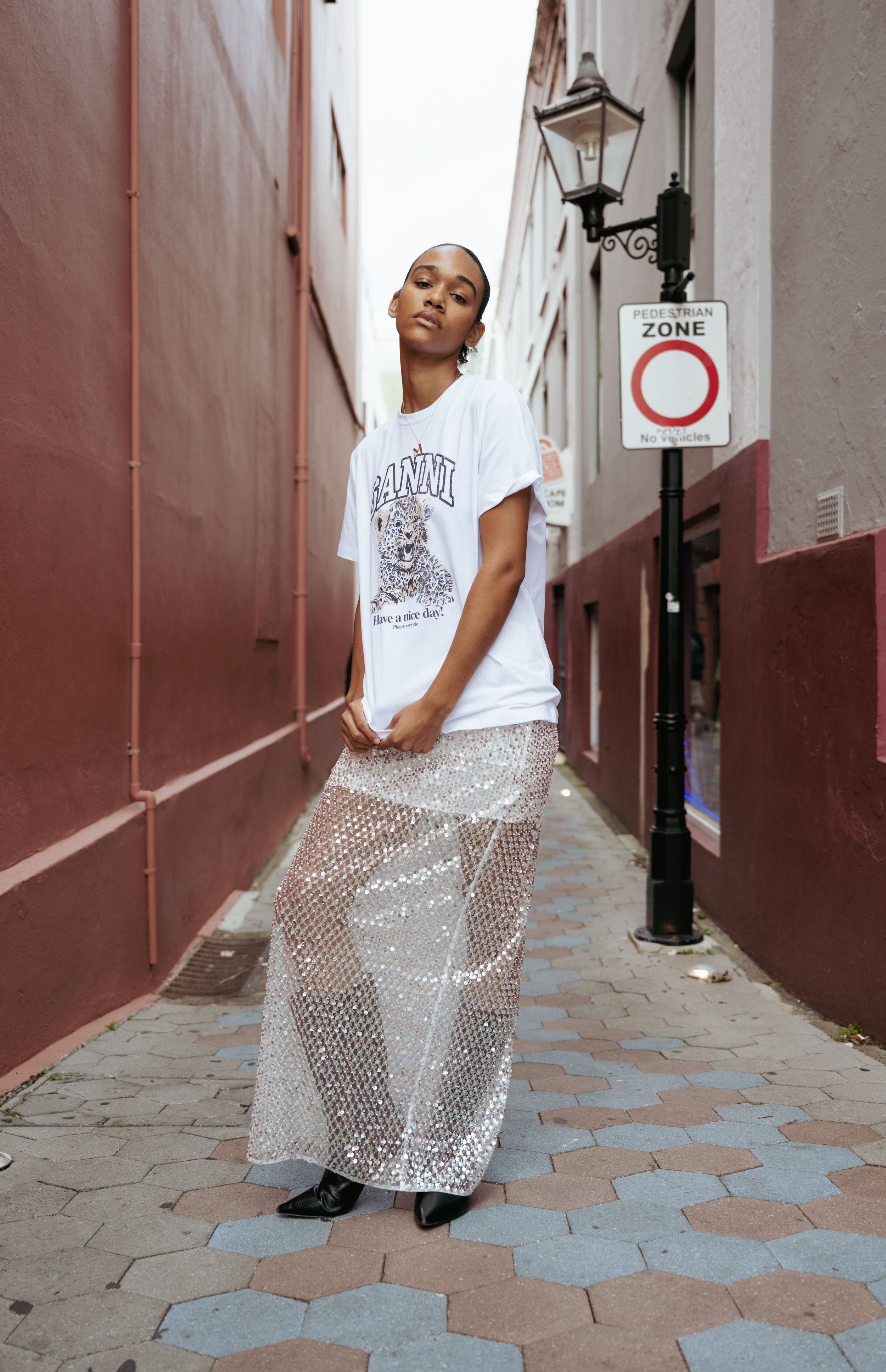 Street style photo featuring graphic tee and sheer patterned pants in urban alleyway.