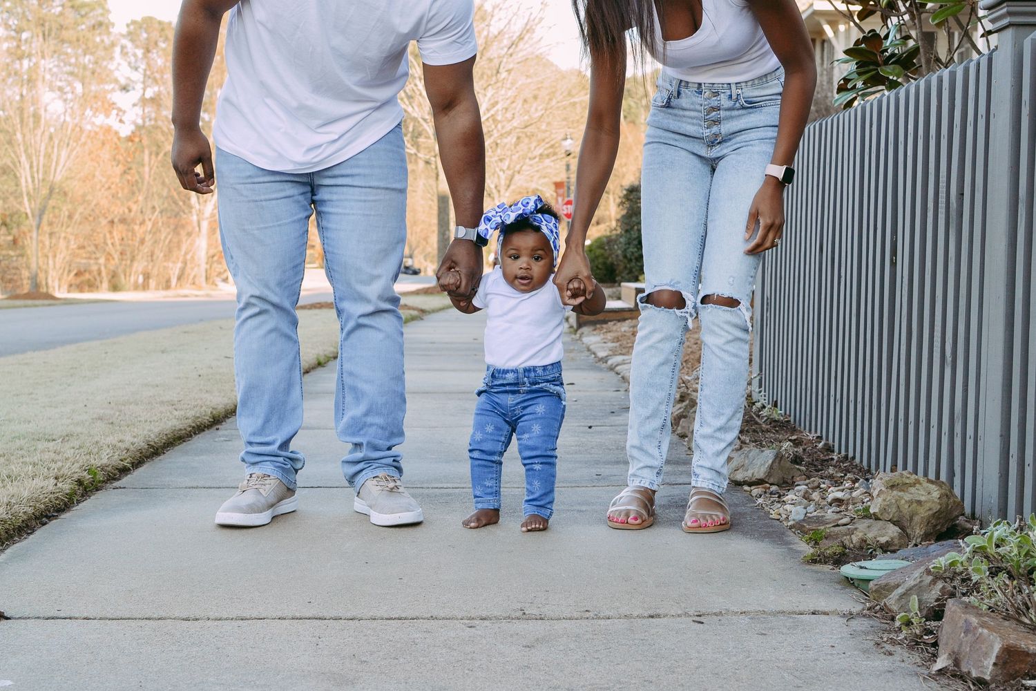 Family wearing matching denim walking together on sidewalk holding hands.
