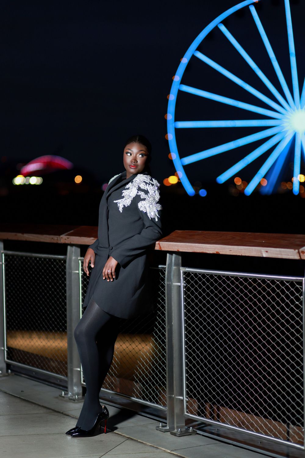 Stylish nighttime portrait with illuminated Ferris wheel in background.