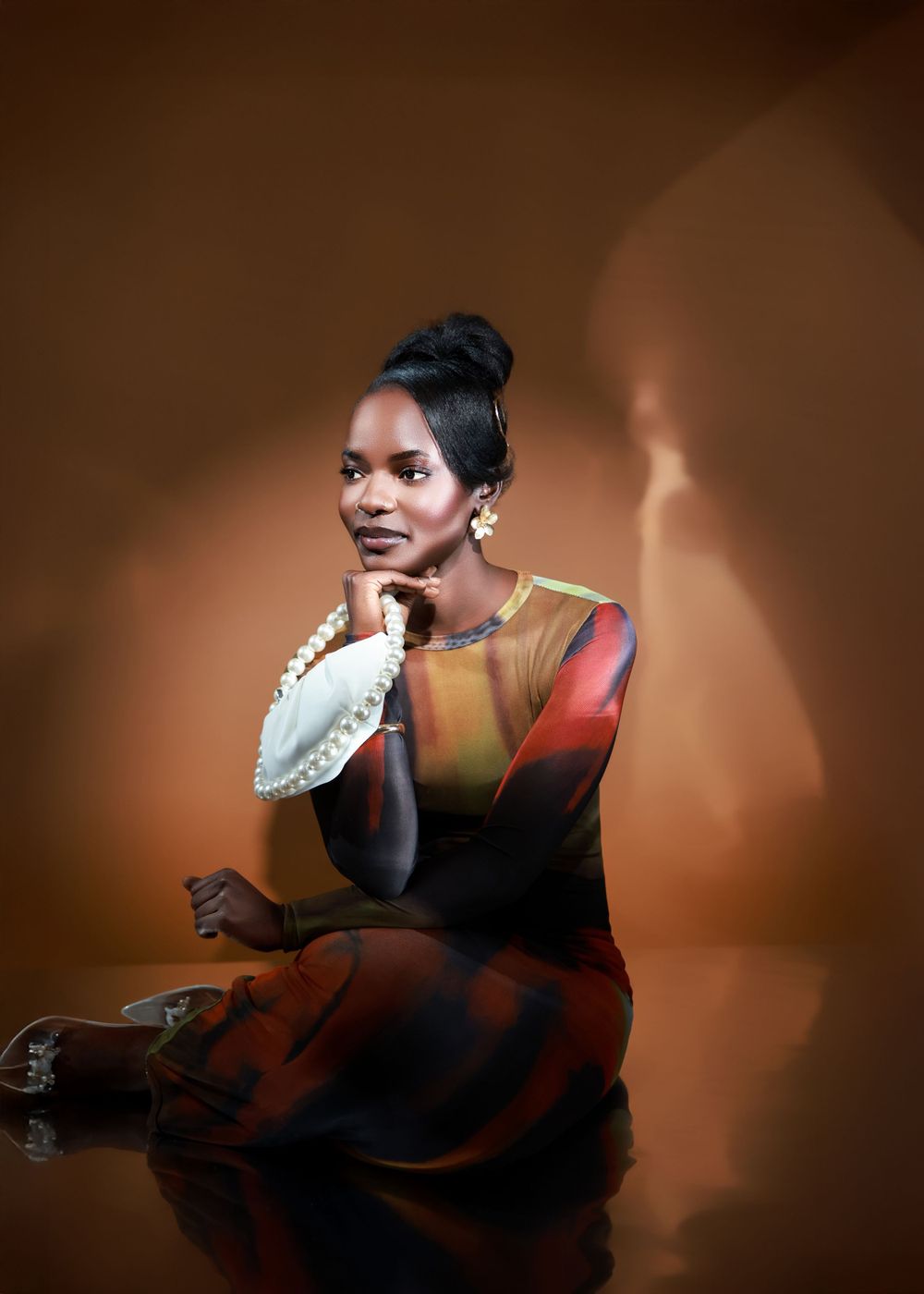 An artistic portrait with dramatic lighting featuring a colorful dress and pearl-handled bag against brown backdrop.