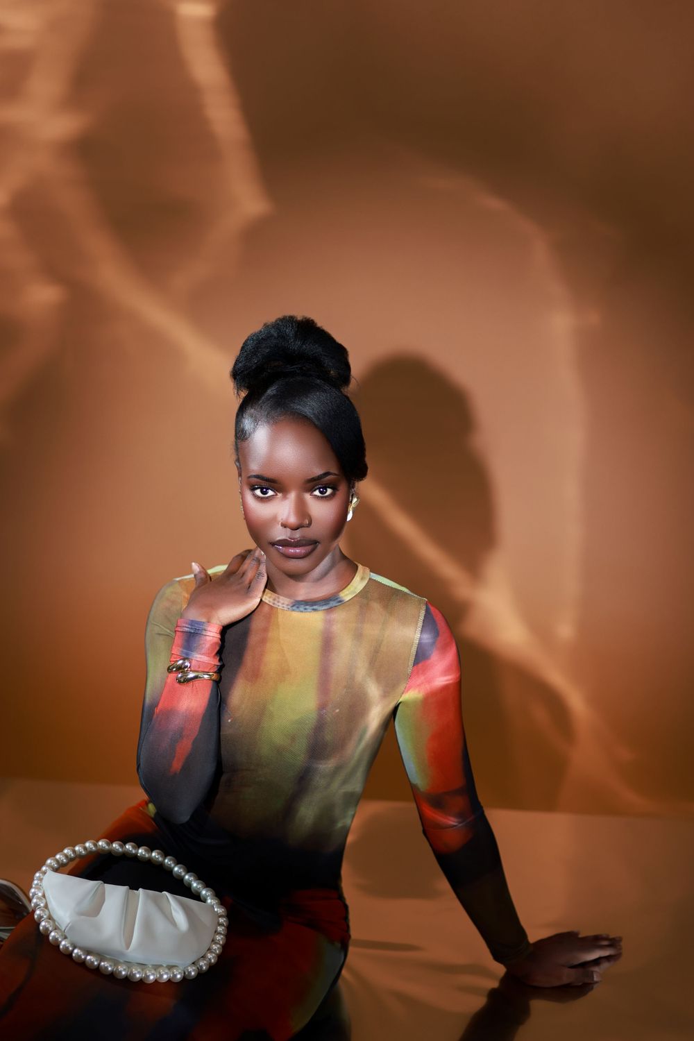 A high fashion portrait with moody lighting showing a colorful fitted dress and statement accessories.