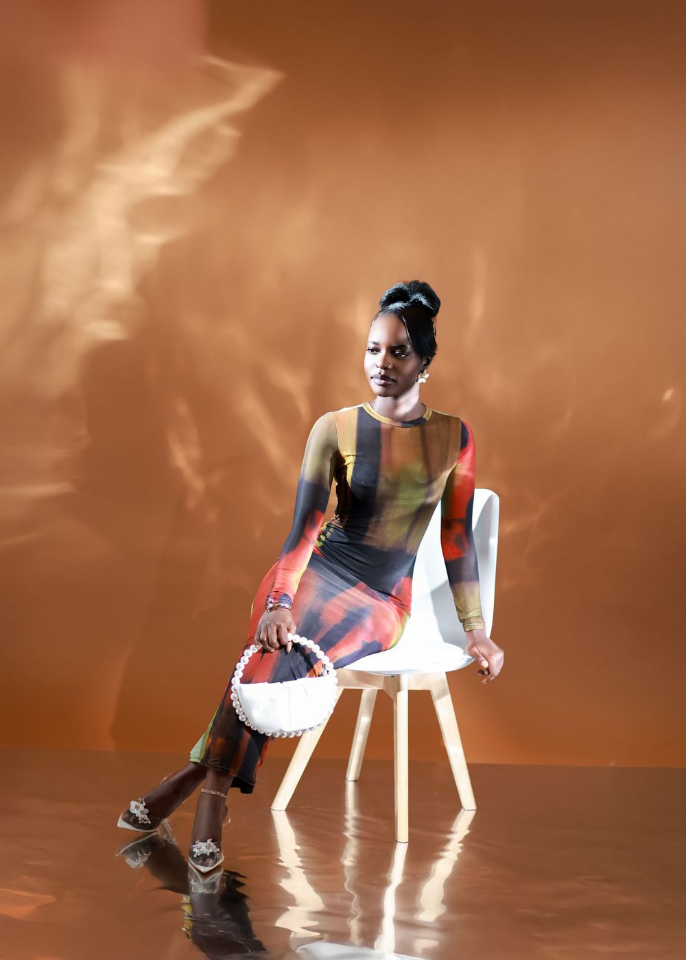 A studio fashion shot on white chair featuring multicolored bodysuit and structured white handbag.